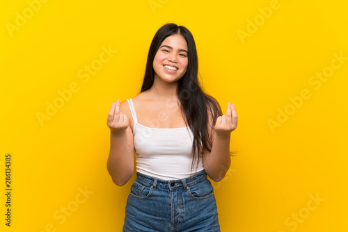Young teenager Asian girl over isolated yellow background making money gesture