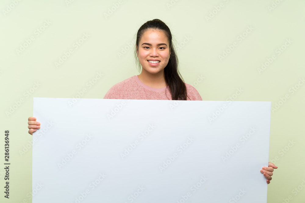 Young teenager Asian girl over isolated green background holding an empty white placard for insert a concept
