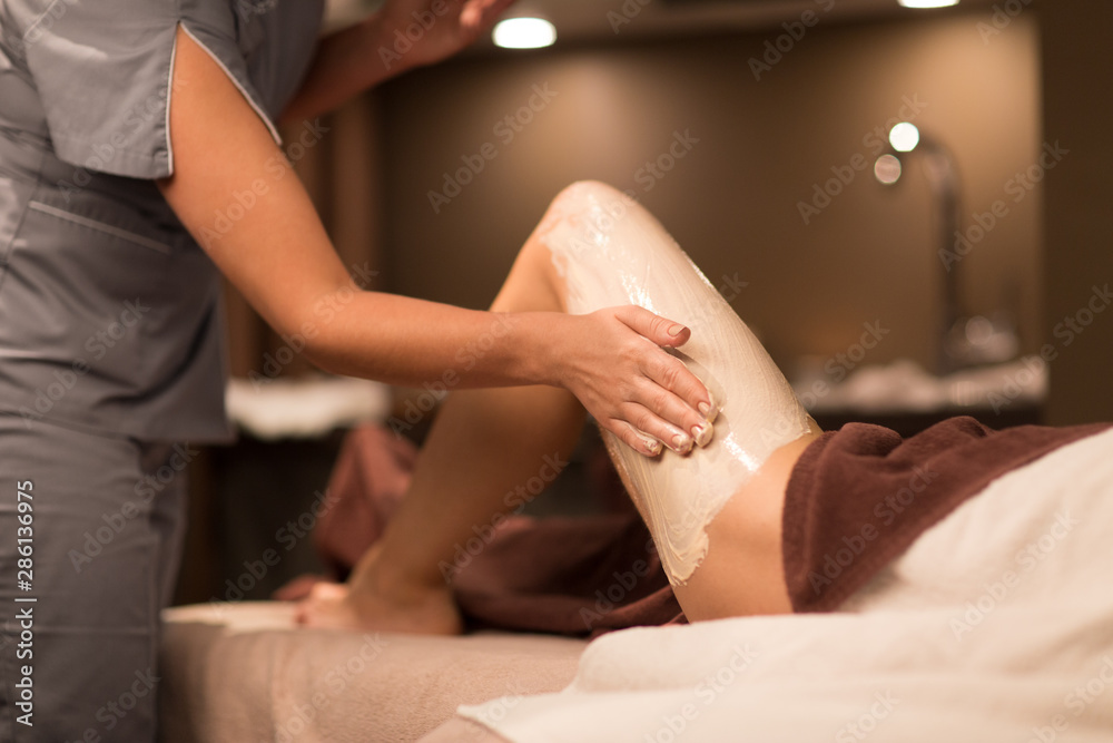 Fototapeta premium beauty, bodycare and luxury concept - close up of beautician applying mask to woman's body at spa
