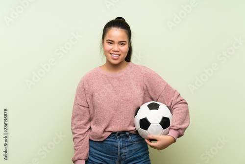 Young teenager Asian girl over isolated green background holding a soccer ball © luismolinero