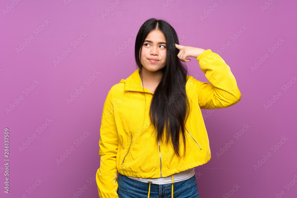 Young teenager Asian girl over isolated purple background making the gesture of madness putting finger on the head