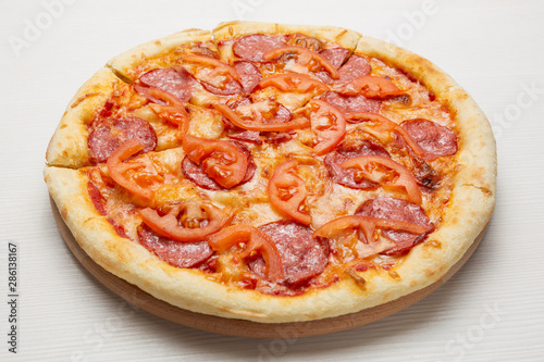 italian pizza with salami sausage, tomatoes and cheese, on a white wooden table