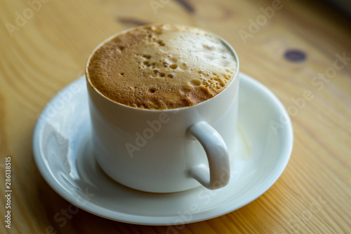 cup of coffee in a white cup stands on a wooden table