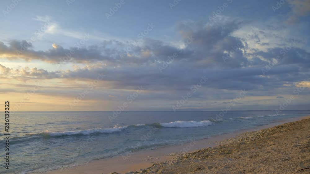 Tropical beach with volcanic rock during low tide waves in sunset with clouds in the sky
