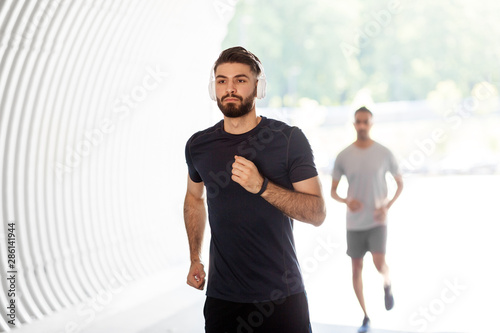 fitness  sport and healthy lifestyle concept - young men or male friends with headphones running outdoors