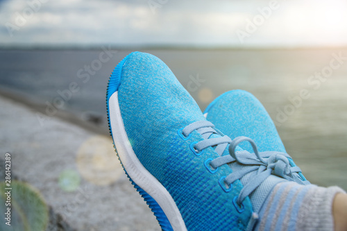 Sporty woman wears blue tying the laces on blue running shoes while taking break between training outside.