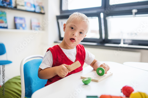 A down-syndrome school boy sitting at the desk in the classroom, learning.