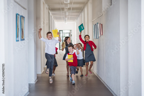 A group of cheerful small school kids in corridor, running and jumping.