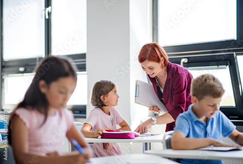 A teacher walking among small school children on the lesson, explaining.