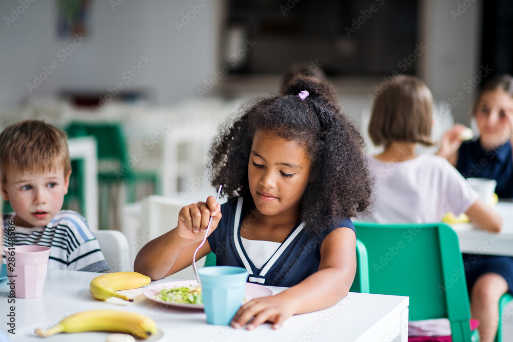 A group of cheerful small school kids in canteen, eating lunch. Stock Photo