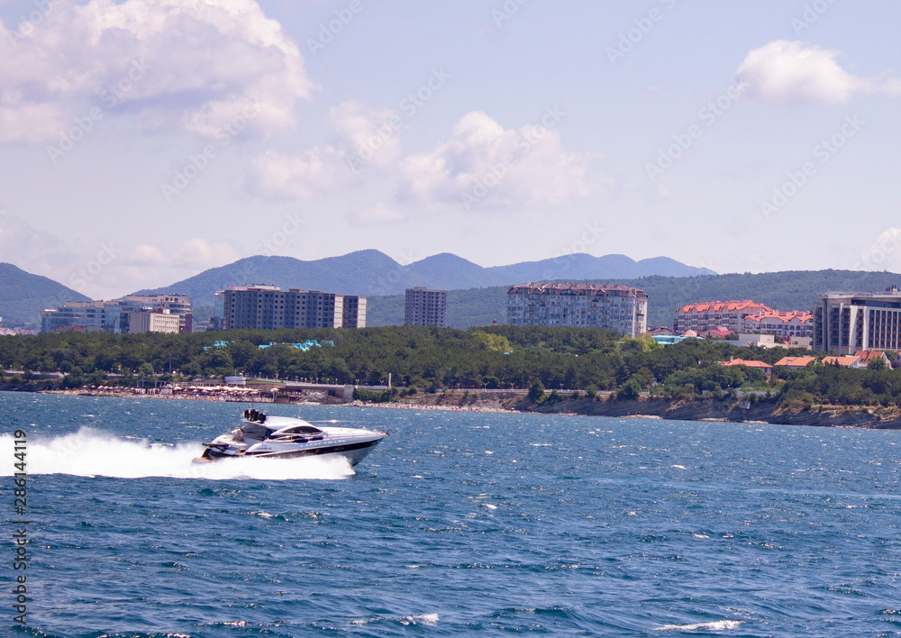 powerboat sails along the coast of the resort town against the backdrop of the mountains on a sunny day
