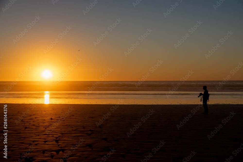 Silhouette of a man with a camera watching the sunset over the Atlantic Ocean from Agadir beach, Morocco, Africa