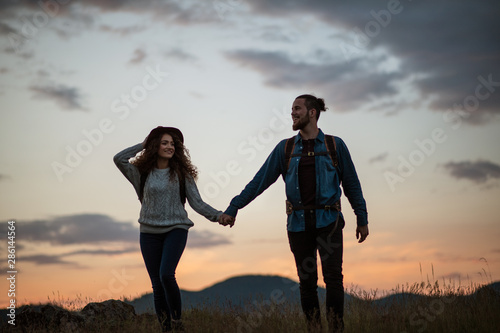 Young tourist couple travellers with backpacks hiking in nature at dusk.