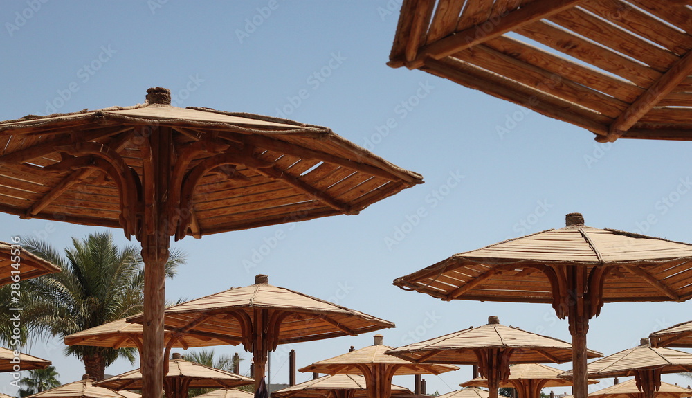 Hats of wooden beach umbrellas against the blue sunny sky in summer