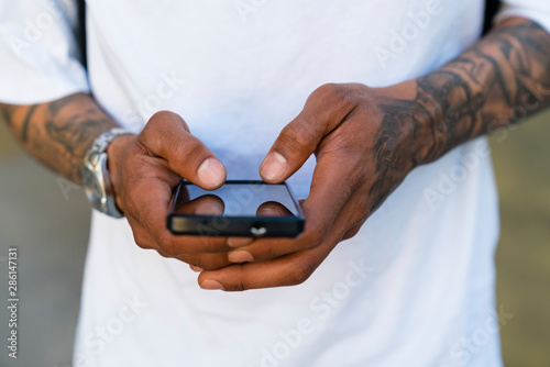 Hands of tattooed man using smartphone  close-up