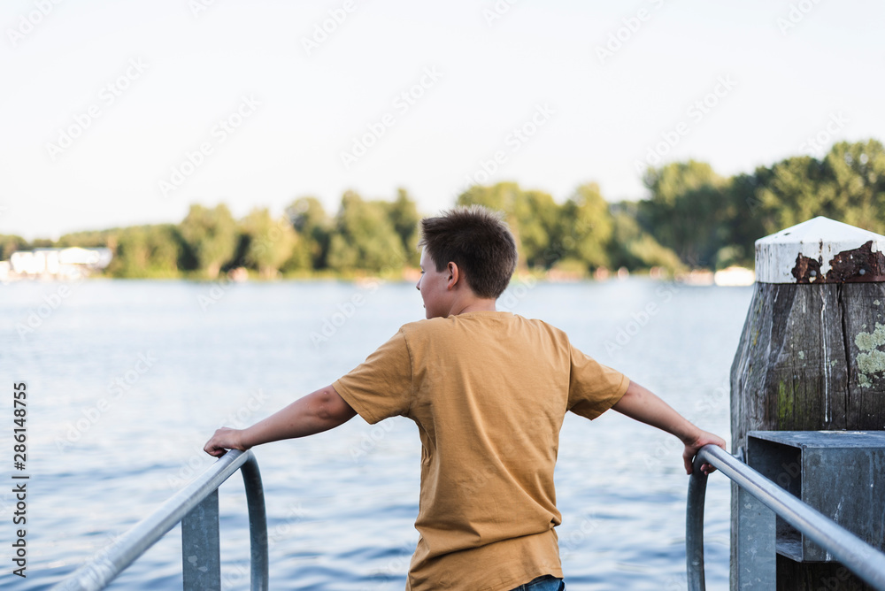 A teenage boy looks at the lake from a pier.