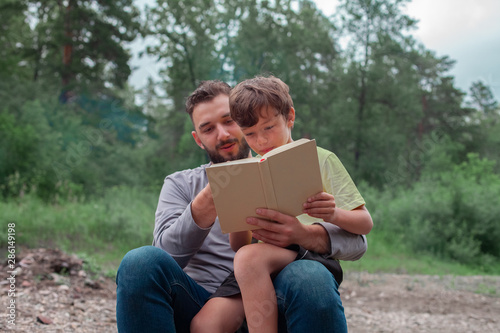 A man with a boy in nature are reading a book. family and fatherhood concept