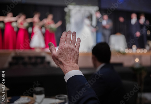 guests and members of the wedding party raise hands as they pray for the bride and groom.