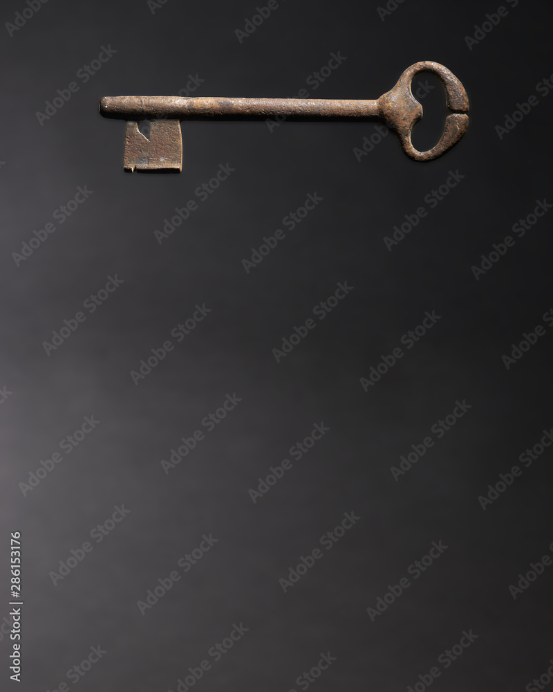 Old key at the top of the page. Security and protection concept. Copy space text. Isolated on dark background. Old key at the top of the page. Security and protection concept. Copy space text. Isolated on dark background.