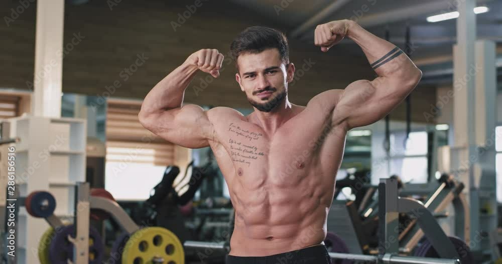 Happy smiling fit man in the gym after the workout exercises flexing his muscle in front of the camera