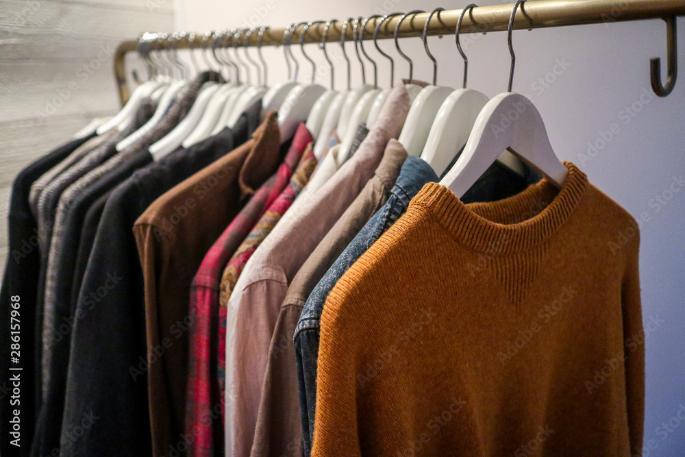 Obraz premium Clothes in the forms of sweaters and shirts of different textile fabrics and colors are haning on hangers on a clothing rack in a bedroom