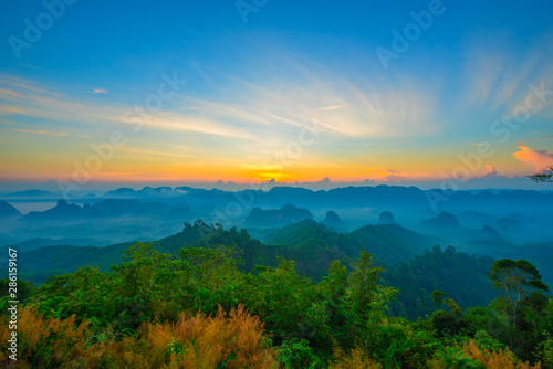 Beautiful mountain range with sky blue and orange light of the sun through the clouds in the morning, Background sky during Sunrise with fog on mountain, Abundant lush forest-Image