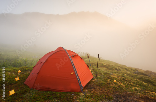 Tourist red tent in mysty mountains at sunrise