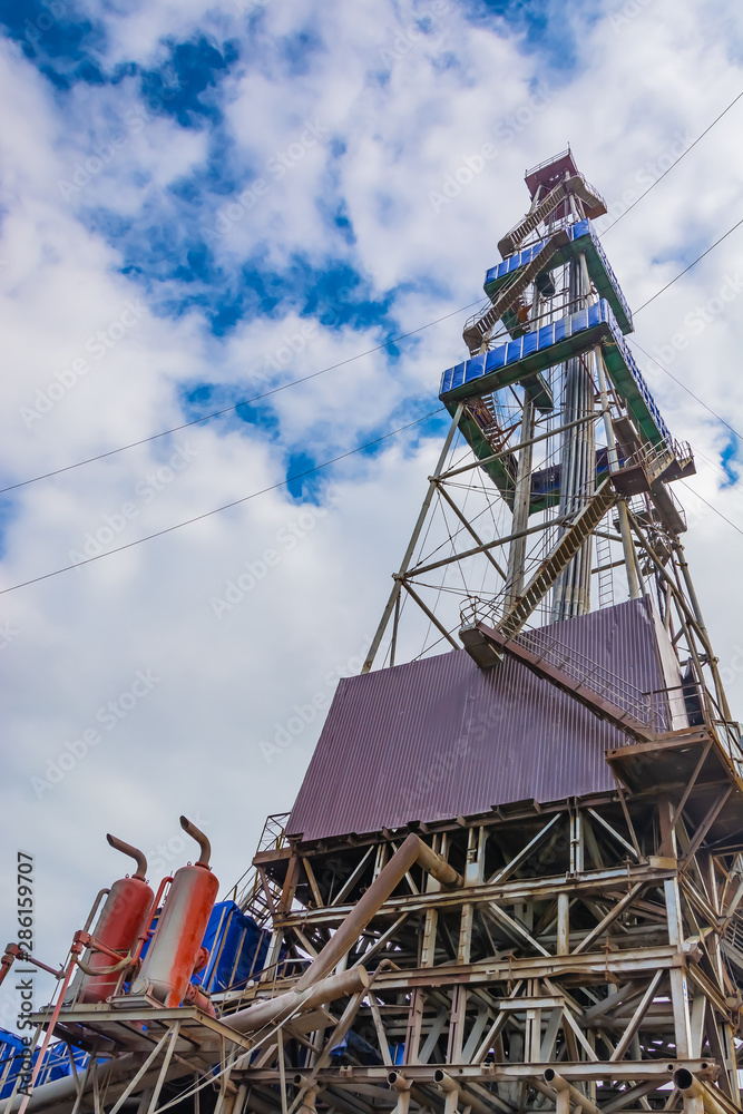 Drilling rig with a tower tower. Downstairs is the drilling equipment. A deep well is being drilled in the northern field for oil and gas production. Summer day. Blue cloudy sky. Drilling rig with a tower tower. Downstairs is the drilling equipment. A deep well is being drilled in the northern field for oil and gas production. Summer day. Blue cloudy sky.