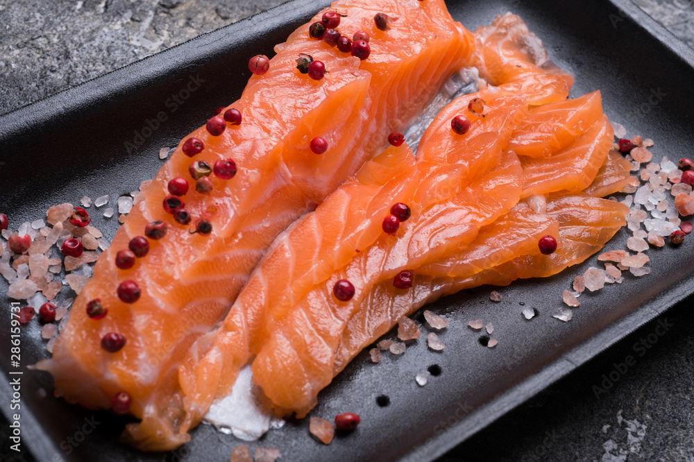 Raw fillet of salmon. Fresh salted and beautiful salmon fillet on black plate. Delicious fish meat. close up Raw fillet of salmon. Fresh salted and beautiful salmon fillet on black plate. Delicious fish meat. close up