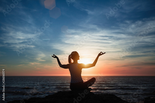 Meditation girl yoga silhouette on the ocean beach during fantastic sunset.