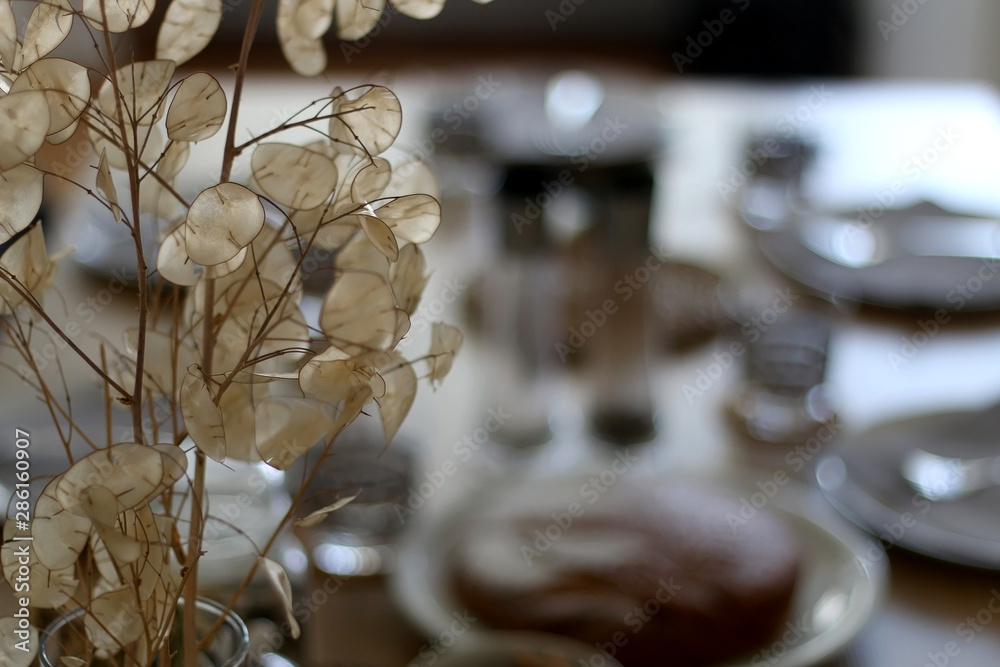 Vase with dry flowers on the table, with dishware and served food in the background. Selective focus.
