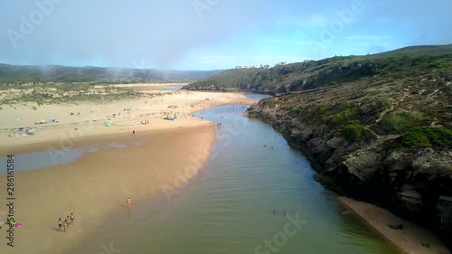 Aerial, drone shot, over people and the coast of the Praia da Amoreira beach, in Aljezur, on a foggy morning, at the Atlantic sea, Vicentine coast national park, in Algarve, Portugal