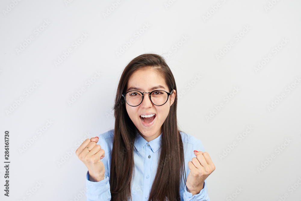 Clever young Asian student girl with glasses and smiles and screams with happiness, clenching fists on white background isolated. Kazakh schoolgirl passed exams perfectly, enjoys holidays and success Clever young Asian student girl with glasses and smiles and screams with happiness, clenching fists on white background isolated. Kazakh schoolgirl passed exams perfectly, enjoys holidays and success