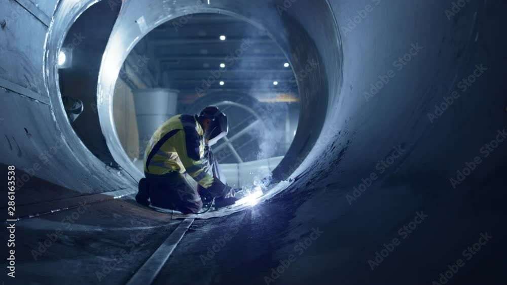 Professional Heavy Industry Welder Working Inside Pipe Wears Helmet and Starts Welding. Construction of the Oil, Natural Gas and Fuels Transport Pipeline. Industrial Manufacturing Factory. Slow Motion