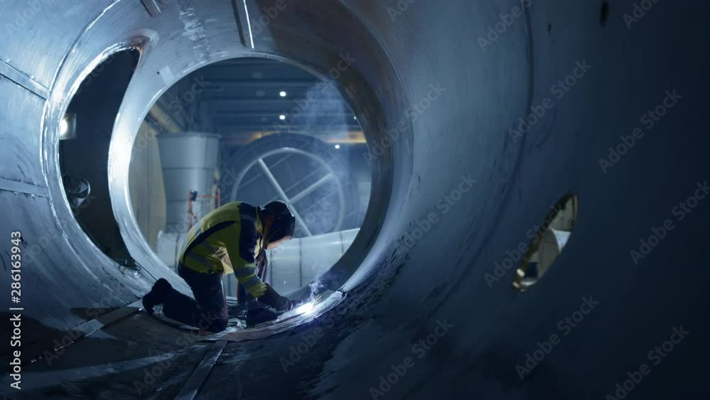 Professional Heavy Industry Welder Working Inside Pipe, Wears Helmet and Starts Welding. Construction of the Oil, Natural Gas and Fuels Transport Pipeline. Industrial Manufacturing Factory