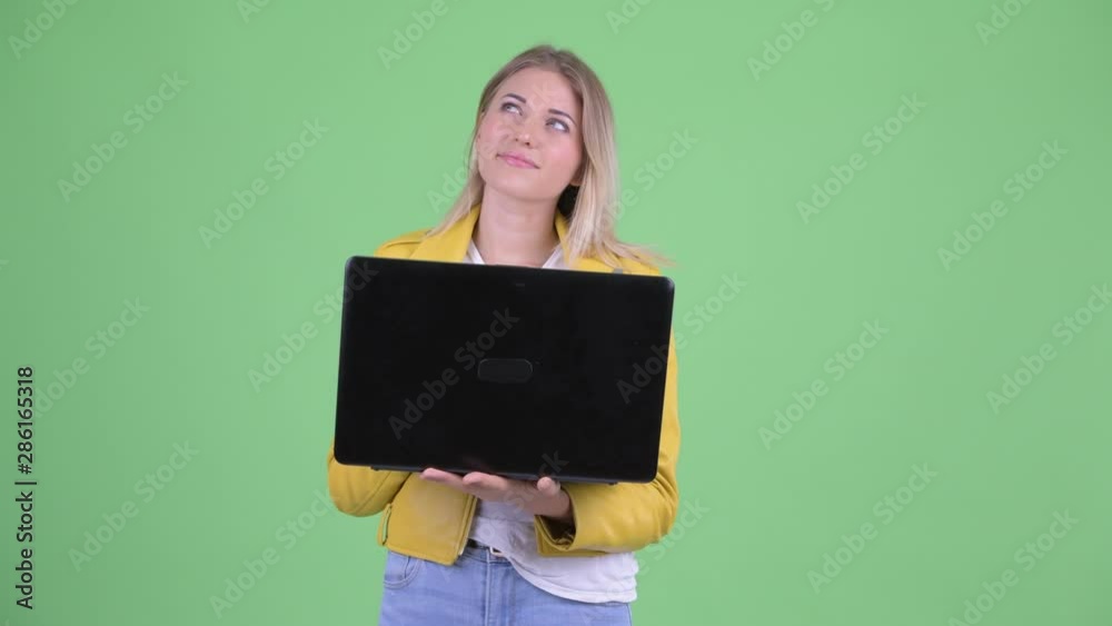 Happy young rebellious blonde woman thinking while using laptop Happy young rebellious blonde woman thinking while using laptop