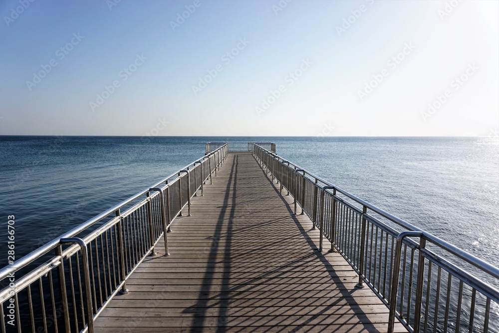 Empty old wooden pier over blue sea with clear cloudless sky background at day time.