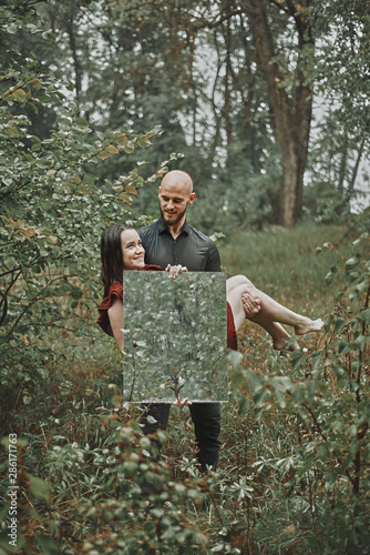 young guy holds a girl in his arms. woman holds a mirror in the forest in the raint. concept of vomiting, love, feelings, soul. photo