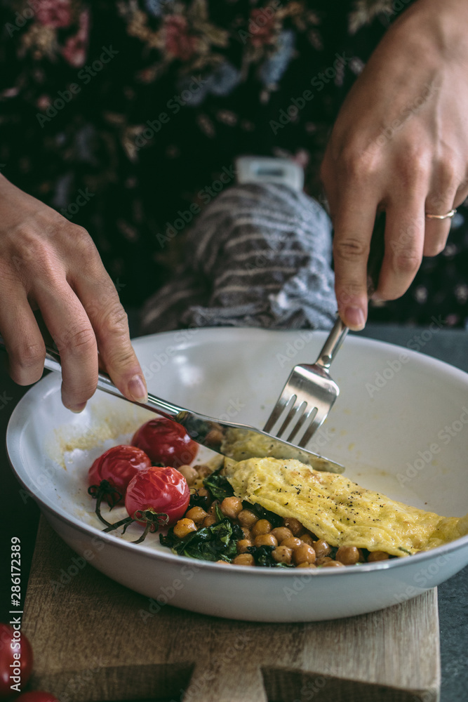 Yellow omelette with chick peas, spinach, cheese and roasted heirloom cherry tomatoes in white frying pan