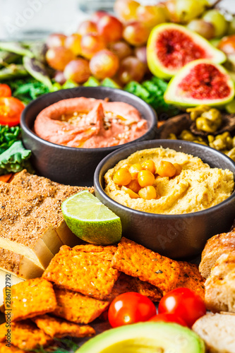Vegan appetizer platter. Hummus, tofu, vegetables, fruits and bread on black tray.