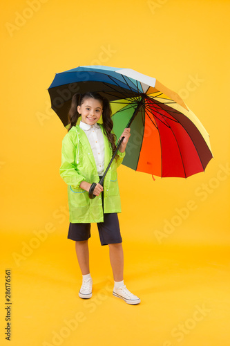 Carefree schoolgirl colorful umbrella wear waterproof rain coat. Autumn rain. Going to school rainy days more fun with bright accessories. Rain is not so bad if you have water resistant clothes