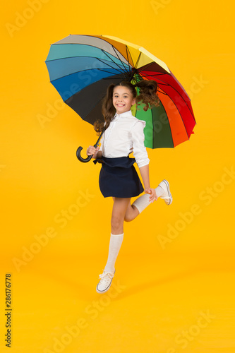 Back to school on September 1. Adorable schoolgirl with rainbow umbrella on September 1 on yellow background. Small child going to school on September 1. Little girl at first school day, September 1