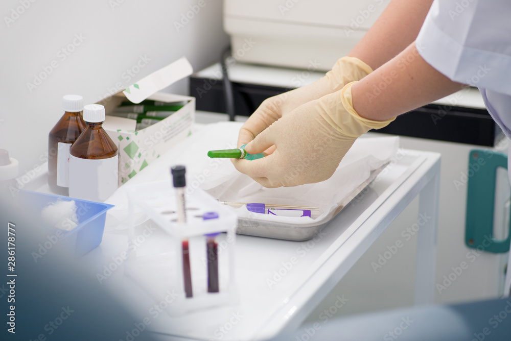 gloved laboratory assistant preparing for blood sampling against a background of blood tubes gloved laboratory assistant preparing for blood sampling against a background of blood tubes