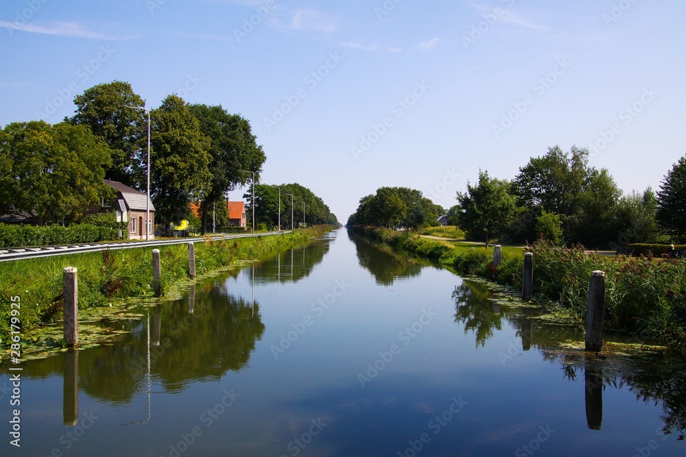 View on typical dutch endless straight waterway canal lined with green grass and trees in countryside - Netherlands, Limburg between Roermond and Venlo