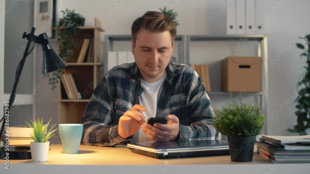 Young man seat in office table and using smartphone. Using ethernet technology at night in work. 4k slow motion footage. Young man seat in office table and using smartphone. Using ethernet technology at night in work. 4k slow motion footage.