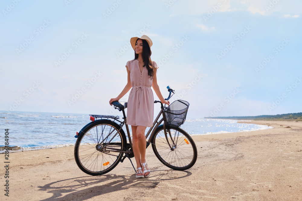 Young beautiful woman is enjoying summer with her bicycle at the seaside on the bright sunny day.