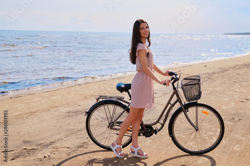 Young beautiful woman is enjoying summer with her bicycle at the seaside on the bright sunny day.