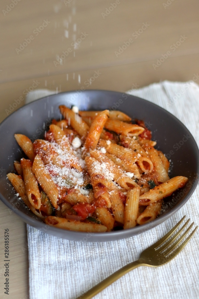Sprinkling parmesan cheese on a plate of pasta with tomato sauce and eggplant. Selective focus. Sprinkling parmesan cheese on a plate of pasta with tomato sauce and eggplant. Selective focus.