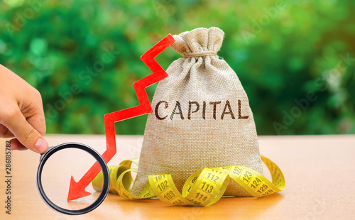 Money bag with the word Capital and arrow down. Fall in the level of authorized capital. Drop in return on equity. The export of fund abroad in order to more reliable and profitable investment. photo