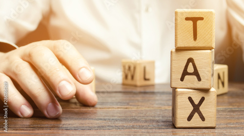 Wooden blocks with the word tax and a businessman sitting at the table. Making the right decision. Time to pay taxes. The concept of annual taxation. Taxes on vehicles, property, purchases. State fee